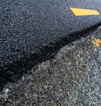 Old verses new look at a resurfaced lanes of a worn road compared to newly installed asphalt, The old road surface is worn, cracked and crumbling, the yellow lines are barely visible, compared to the newly laid asphalt